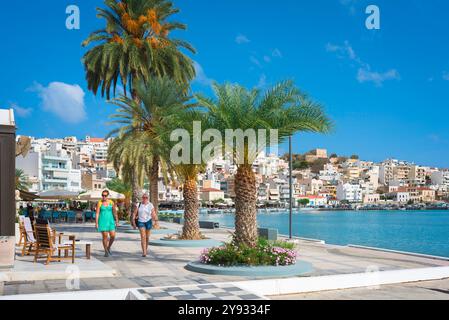 Griechenland Urlaub, Blick auf zwei junge Frauen, die entlang der Palmen gesäumten Uferpromenade in der Bucht von Sitia, Nordosten Kretas, Griechenland, spazieren gehen Stockfoto