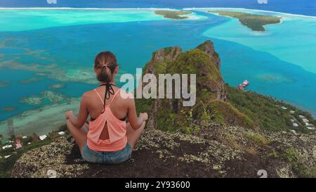 Die junge Frau übt Yoga und genießt einen Moment der Ruhe, während sie die malerische Aussicht auf die Lagune der Insel maupiti in französisch-polynesien bewundert Stockfoto