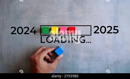 Eine Hand legt einen blauen Block auf eine Ladestange mit farbigen Blöcken, die den Übergang von 2024 zu 2025 darstellen. Neues Jahr, neues Startkonzept. Stockfoto