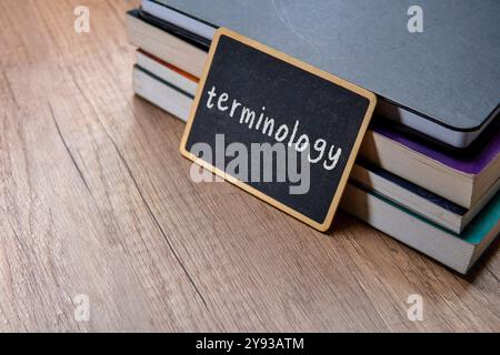 Eine Tafel mit dem Wort „TERMINOLOGIE“ wird auf einen Stapel Lehrbücher auf einem Holztisch gelegt. Kopierbereich für Text. Stockfoto