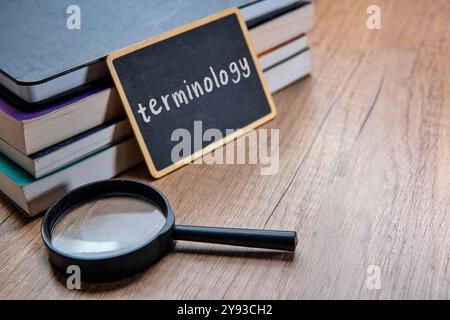 Eine Tafel mit dem Wort „TERMINOLOGIE“ wird auf einen Stapel Lehrbücher auf einem Holztisch gelegt. Kopierbereich für Text. Stockfoto