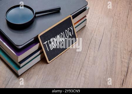 Eine Tafel mit dem Wort „TERMINOLOGIE“ wird auf einen Stapel Lehrbücher auf einem Holztisch gelegt. Kopierbereich für Text. Stockfoto