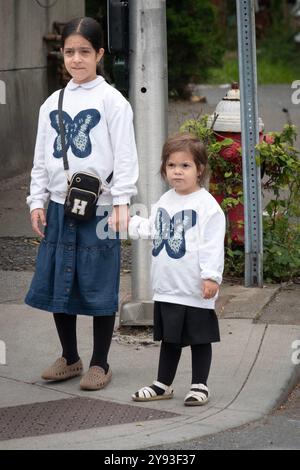 Bescheiden gekleidete orthodoxe jüdische Schwestern gehen Hand in Hand, während sie denselben Schmetterlingspullover tragen. Im Rockland County, New York, 2024. Stockfoto