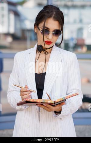 Eine modische Geschäftsfrau in gestreiftem Anzug mit Sonnenbrille im Notizblock im Freien. Stockfoto