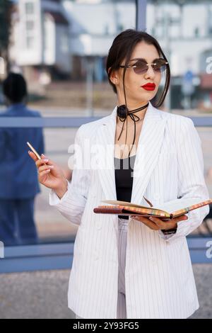 Stilvolle Geschäftsfrau in schickem gestreiften Blazer mit Notebook und Sonnenbrille. Stockfoto