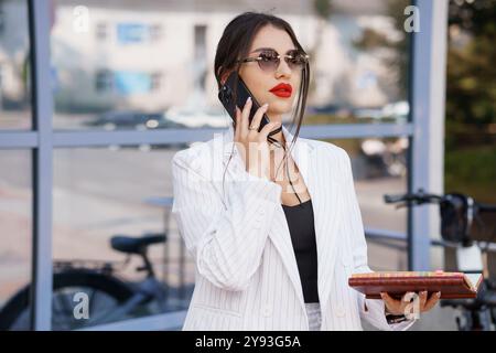 Stilvolle Geschäftsfrau mit Sonnenbrille und Smartphone in einem modernen urbanen Ambiente. Stockfoto