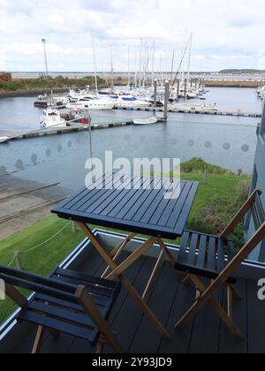 Zimmer mit Blick: Terrassentisch und Stühle auf einem Balkon mit Blick auf die Yachten im geschützten Wasser des Yachthafens in Troon Yacht Haven, Schottland. Stockfoto