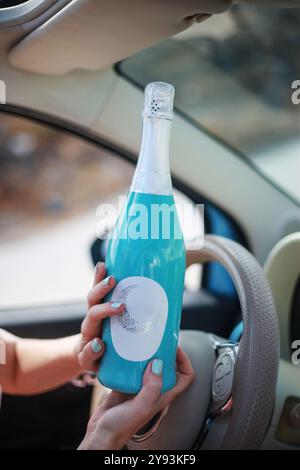 Frau, die eine blaue Flasche mit leerem Etikett im Auto hält. Rosenwein. Vorderansicht mit Kopierraum. Stockfoto