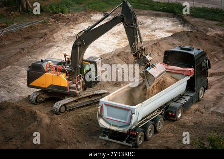 Bagger, der Schmutz in einen Muldenkipper auf einer Baustelle lädt, schöner Blick von oben Stockfoto