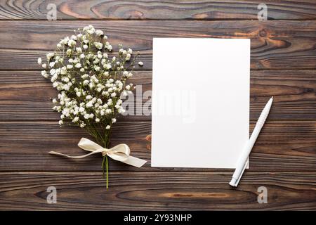 Hochzeitsmodell mit weißer Papierliste und Blumen Zigeuner auf farbigen Tisch Blick flach liegend. Leere Grußkarten und Briefumschläge. Wunderschönes Blumendesign Stockfoto