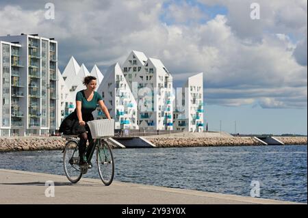 Junge Frau, die mit dem Eisberg-Wohnhaus im Hintergrund radelt, Aarhus, Jütland, Dänemark Stockfoto