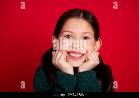 Foto-Porträt des hübschen kleinen Mädchens träumliche Berührung Wangen tragen grüne weihnachten Outfit Mottoparty auf rotem Hintergrund Stockfoto