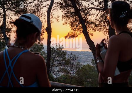 Frauen in Workout-Kleidung genießen den ruhigen Sonnenaufgang über Barcelona von einem malerischen Aussichtspunkt umgeben von Kiefern. Beide schauen vom Camer weg Stockfoto