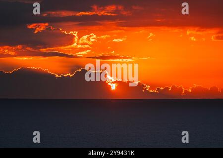 Ein atemberaubender Blick auf einen Sommersonnenaufgang mit feurigen Tönen über die ruhigen Meere von Cullera, Valencia, die den Horizont mit einem warmen Leuchten verschönern. Stockfoto