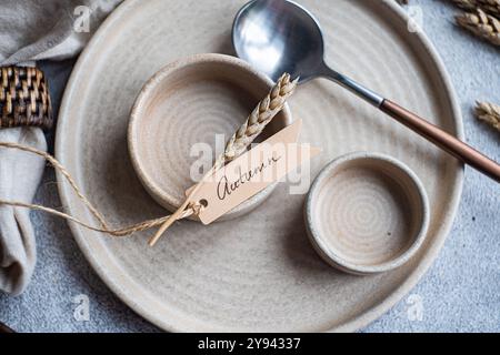 Nahaufnahme einer herbstlich inspirierten Tischplatte mit Weizenstielen, Keramikgeschirr, einem rustikalen Pfeilschild mit der Aufschrift „Herbst“ und natürlichen Texturen von l Stockfoto