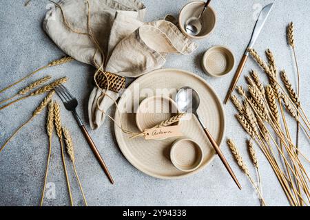 Eine sorgfältig gestaltete Herbsttisch-Einrichtung mit rustikalem Weizenmotiv in neutralen Tönen und Holzbesteck wird durch Weizenstämme ergänzt Stockfoto