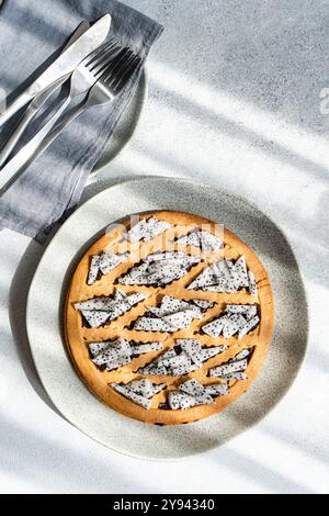 Eine frisch gebackene Drachenfrucht-Tarte auf einer gesprenkelten Keramikplatte, begleitet von Geschirr auf einer strukturierten Oberfläche, beleuchtet von natürlichem Sonnenlicht Stockfoto