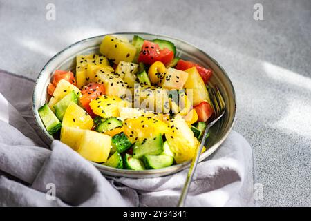 Von oben ein bunter Gemüsesalat mit roten und gelben Tomaten, Gurkenscheiben, Paprika-Stücken und Sesamsamen in einer Metallschale, präsentiert o Stockfoto