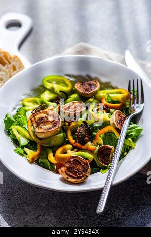 Ein gesunder heißer Salat mit gegrillten weißen Mini-Auberginen-Hälften, frisch geschnittenen grünen Paprika, knusprigen gebratenen Zwiebelringen und frischem Kopfsalat Stockfoto