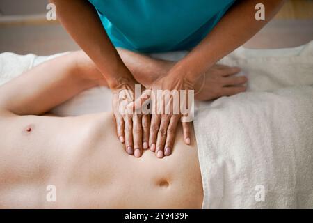 Von oben ein Bild, das eine nicht erkennbare Therapeutin zeigt, die einem männlichen Kunden zu Hause eine entspannende Massage gibt. Der Therapeut verwendet sanfte, Stockfoto