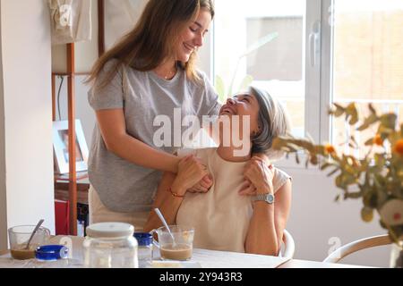 Eine herzerwärmende Szene, in der Mutter und Tochter sich gegenseitig amüsieren, lachen und umarmen in einer sonnigen Küche Stockfoto