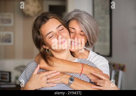 Eine herzerwärmende Szene einer Mutter mit grauem Haar und ihrer Tochter, die sich liebevoll umarmt, beide in gemütlicher Atmosphäre sanft lächeln Stockfoto