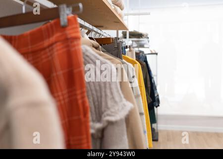 Eine Auswahl moderner Freizeitkleidung, darunter gemusterte Röcke und gemütliche Pullover, die in einer hellen, luftigen Boutique auf Kleiderbügeln angebracht sind Stockfoto