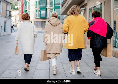 Vier Frauen mittleren Alters laufen die Straße entlang, jede trägt Einkaufstaschen und trägt stilvolle Herbstkleidung und genießt einen gemeinsamen Einkaufstag Stockfoto