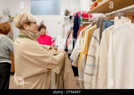 Drei Freundinnen genießen einen Einkaufsbummel in einer gemütlichen Boutique und stöbern durch die Regale voller modischer Kleidung Stockfoto