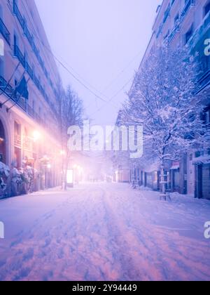Eine ruhige Winterszene in Madrid, Spanien, mit Schnee über den Straßen und Bäumen unter dem Dämmerungshimmel, beleuchtet von den warmen Lichtern Stockfoto