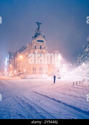 Ein ruhiger nächtlicher Blick auf die schneebedeckten Straßen in Madrid, Spanien, mit einer Figur in der Nähe der berühmten Architektur, dem Metropolis-Gebäude, beleuchtet von Stockfoto