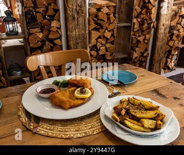 Ein gemütliches Berghütten-Restaurant, das ein traditionelles Schnitzel mit knusprigen Pommes Frites und Obstmarmelade serviert, präsentiert auf rustikalem Holztisch mit Hütte Stockfoto