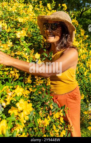 Eine begeisterte Frau mit Strohhut berührt an einem sonnigen Tag in Amsterdam leuchtende gelbe Blüten, ihre Freude gefangen in üppigem Grün Stockfoto