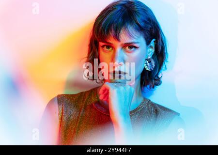 Ein eindrucksvolles Porträt einer jungen Frau mit nachdenklichem Ausdruck, gebadet in mehrfarbigen Lichtern. Ihre auffälligen Merkmale werden durch ein auffälliges Make-up hervorgehoben Stockfoto