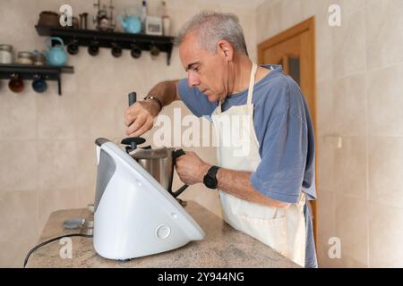 Ein Mann mittleren Alters konzentriert sich intensiv, während er mit einer modernen Küchenmaschine Zutaten für einen Three Kings Cake in gemütlicher Atmosphäre mischt Stockfoto