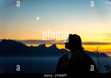 Seitenansicht einer nicht erkennbaren Silhouette der Frau, die einen atemberaubenden Sonnenuntergang in den Schweizer Alpen in der Nähe des Genfer Sees mit lebhaften Himmelsfarben und Bergen bestaunt Stockfoto