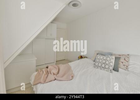 Ein ordentlich organisiertes Schlafzimmer auf dem Dachboden mit einem komfortablen Bett, einer schrägen Decke und eingebauten Abstellschränken für eine ruhige und gemütliche Atmosphäre. Stockfoto