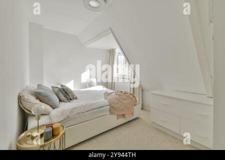 Ein gut beleuchtetes Schlafzimmer im Dachgeschoss mit einem komfortablen Bett, modernen Möbeln und minimalistischer Einrichtung unter einer schrägen Decke. Stockfoto