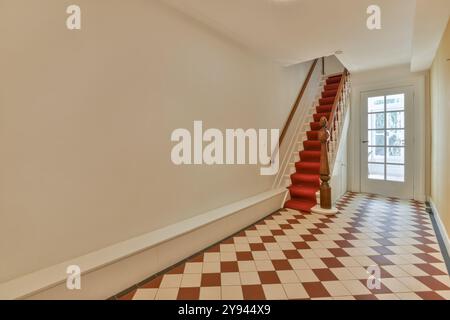 Ein stilvolles Interieur mit einem hellen Flur mit einer Treppe mit rotem Teppichboden und einem klassischen karierten Boden. Stockfoto