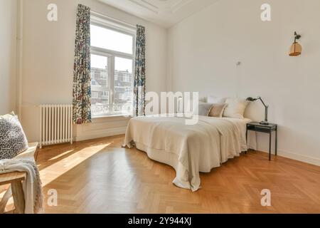 Ein geräumiges und gut beleuchtetes Schlafzimmer mit großem Fenster, Hartholzboden und minimalistischer Einrichtung mit eleganten Vorhängen. Stockfoto