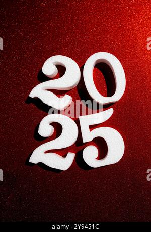 Weiße 3D-Zahlen 2025 vor einem leuchtend roten Glitzerhintergrund, die die feierliche Essenz des neuen Jahres festhalten. Stockfoto