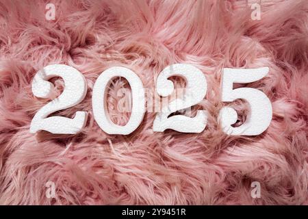 Ein lebendiges und strukturiertes Display mit den Zahlen 2025 in kräftiger, weißer Textur vor flauschigem, rosafarbenem Kunstpelzhintergrund, ideal für Silvester-Grafiken. Stockfoto