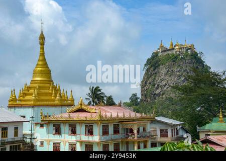 Der mit Golden Stupa geschmückte Mount Popa bildet einen majestätischen Hintergrund über der traditionellen birmanischen Architektur im Vordergrund, unter einem blauen Himmel. Stockfoto