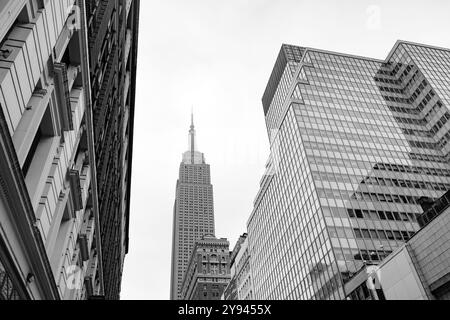 Ein beeindruckendes Schwarzweißfoto, das die architektonische Vielfalt von New York City feststellt. Das Empire State Building erhebt sich majestätisch zwischen verschiedenen anderen Gebäuden Stockfoto