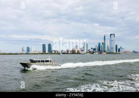 Ein Motorboot rastet auf dem Hudson River entlang und schafft so Wake, mit der Skyline von New York City im Hintergrund. Wolkenkratzer erheben sich gegen einen bewölkten Himmel, reflektieren Stockfoto