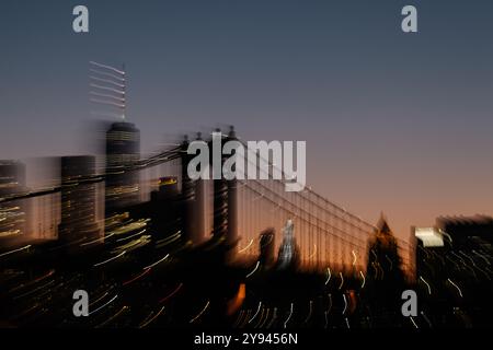 Eine verschwommene und künstlerische Aufnahme der Brooklyn Bridge mit der Skyline von Manhattan in der Abenddämmerung. Die sanften Lichter der Stadt und der sich vertiefende Abendhimmel c Stockfoto