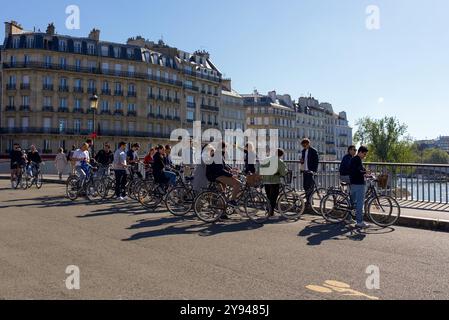 Ein Reiseleiter mit einer Gruppe von Touristen auf Fahrrädern, die Paris an einem sonnigen Herbsttag erkunden. Die Gruppe steht auf einer Brücke über die seine Stockfoto