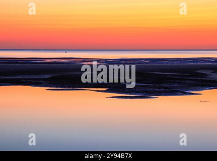 Muster aus dunklem Sand mit dem Nachglühen eines bunten Sonnenuntergangs, der sich bei Ebbe im Wasser spiegelt Stockfoto