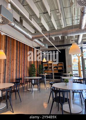 Modernes Café mit eleganten Möbeln, Holzpaneelwänden und industrieller Deckengestaltung mit einzigartiger Beleuchtung. Stockfoto