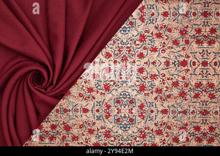 Eine detaillierte Ansicht von rotem Stoff neben einem traditionellen persischen Teppich mit Blumenmustern, kräftigen Texturen und lebhaften Farben. Stockfoto